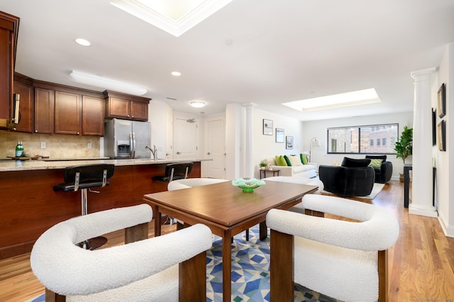 dining area with sink, a skylight, decorative columns, and light wood-type flooring