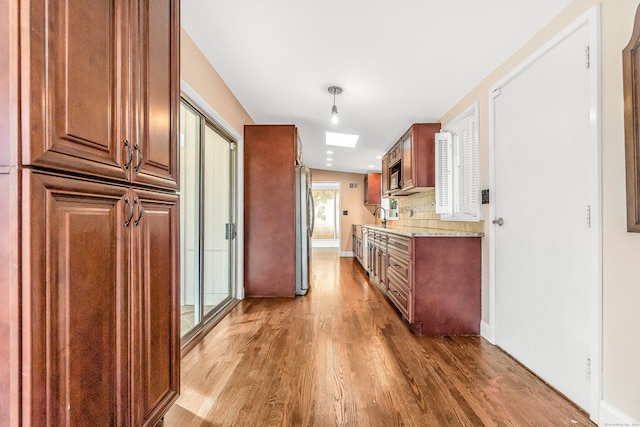 kitchen featuring tasteful backsplash, light stone counters, a skylight, sink, and hardwood / wood-style floors