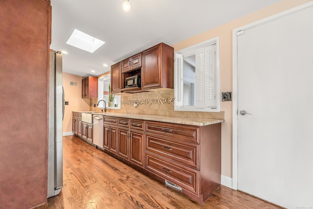 kitchen featuring light stone countertops, a skylight, light hardwood / wood-style flooring, dishwasher, and stainless steel refrigerator