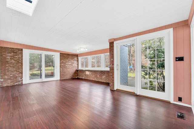 unfurnished living room with dark hardwood / wood-style flooring, vaulted ceiling with skylight, and brick wall