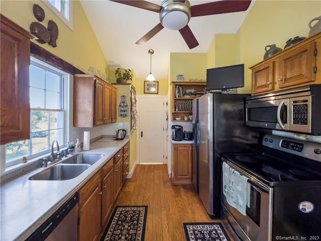 kitchen featuring pendant lighting, lofted ceiling, sink, light hardwood / wood-style flooring, and stainless steel appliances