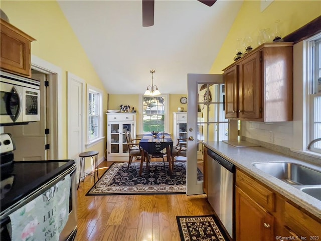 kitchen with pendant lighting, lofted ceiling, sink, light hardwood / wood-style flooring, and stainless steel appliances