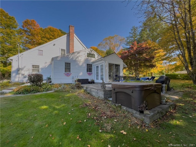 rear view of house with a lawn, a patio area, french doors, and a hot tub