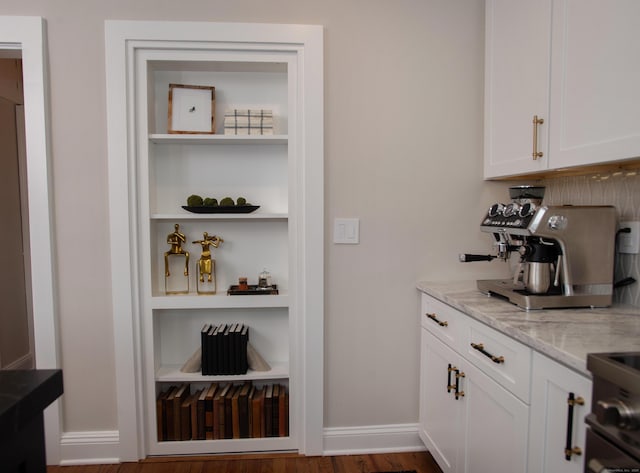 bar featuring white cabinets, built in shelves, light stone countertops, and dark wood-type flooring