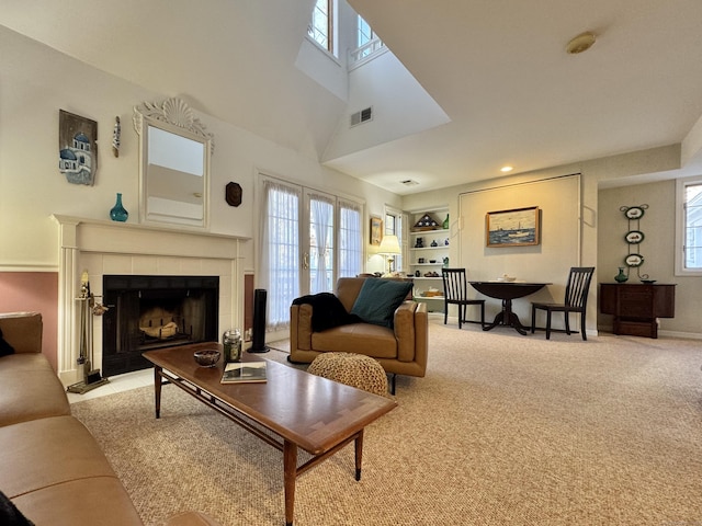 carpeted living room with a tile fireplace, a high ceiling, a skylight, and built in shelves