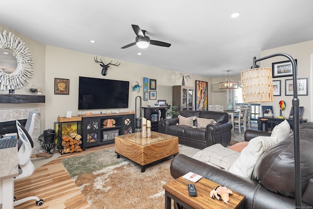 living room featuring a tiled fireplace, wood-type flooring, and ceiling fan with notable chandelier