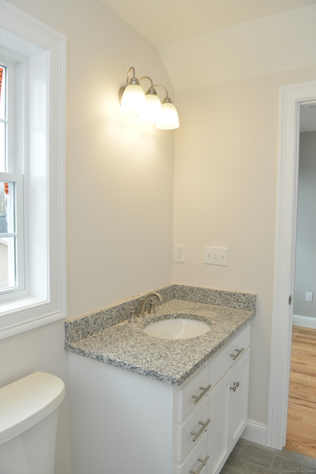 bathroom featuring toilet, vanity, hardwood / wood-style flooring, and vaulted ceiling