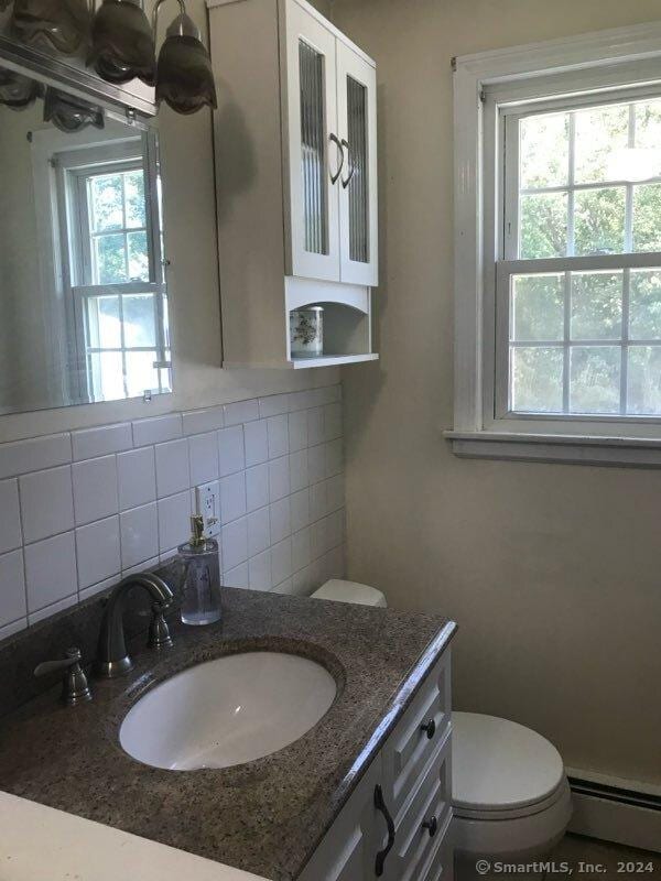 bathroom with backsplash, vanity, a healthy amount of sunlight, and baseboard heating