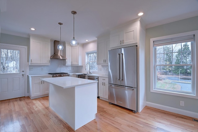 kitchen with stainless steel appliances, white cabinetry, hanging light fixtures, a kitchen island, and wall chimney range hood