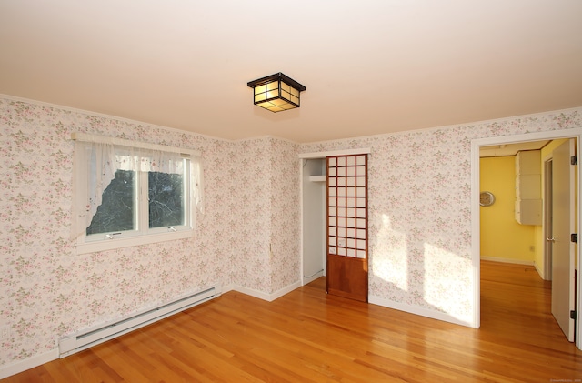 empty room with wood-type flooring, a baseboard radiator, ornamental molding, and a healthy amount of sunlight