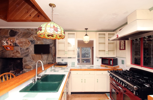 kitchen with sink, hanging light fixtures, ventilation hood, a fireplace, and black appliances