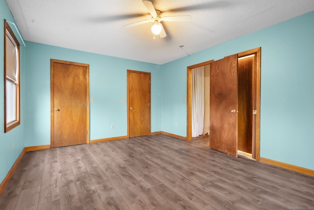 unfurnished bedroom featuring wood-type flooring, a textured ceiling, two closets, and ceiling fan