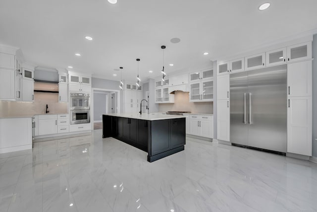 kitchen featuring pendant lighting, backsplash, stainless steel appliances, and a center island with sink