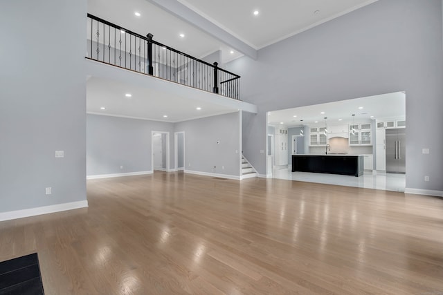 unfurnished living room with crown molding, light hardwood / wood-style flooring, a high ceiling, and sink