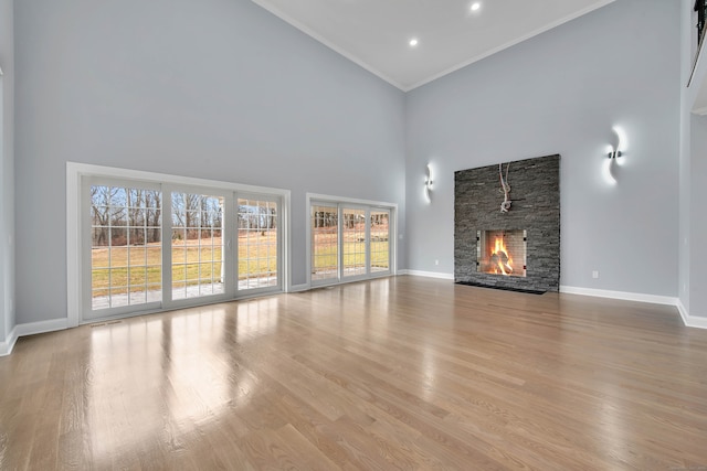 unfurnished living room with light wood-type flooring, a fireplace, a high ceiling, and ornamental molding