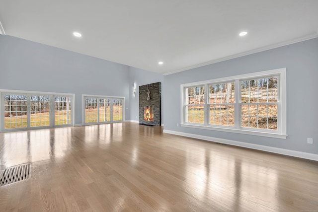 unfurnished living room with light hardwood / wood-style flooring, a stone fireplace, and crown molding