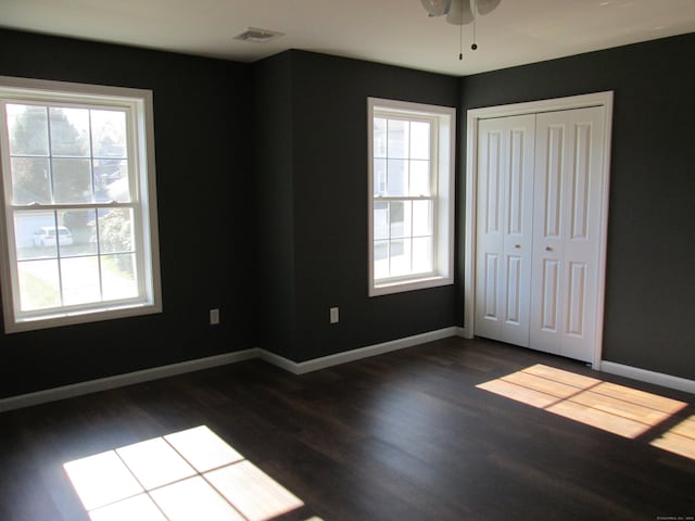 unfurnished bedroom with dark hardwood / wood-style flooring, a closet, and multiple windows