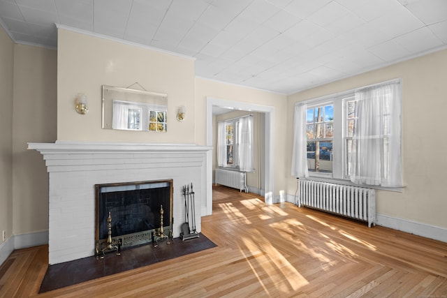 unfurnished living room with parquet flooring, a brick fireplace, radiator, and ornamental molding