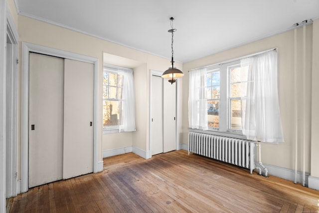 unfurnished bedroom featuring multiple windows, hardwood / wood-style flooring, and radiator