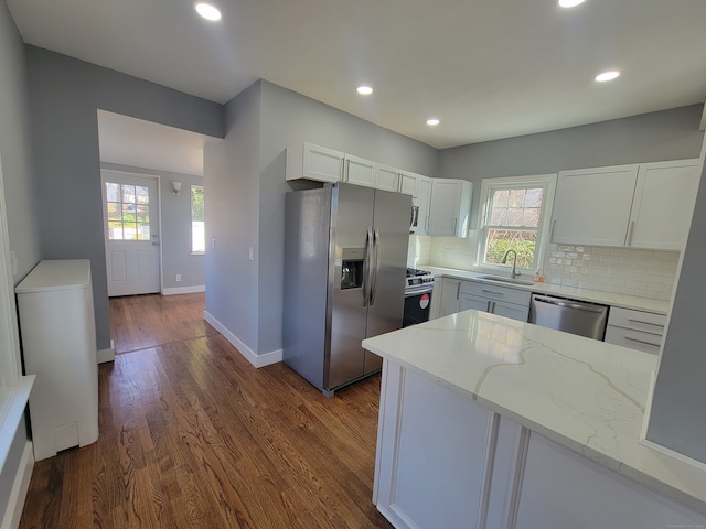 kitchen with light stone countertops, sink, dark wood-type flooring, white cabinets, and appliances with stainless steel finishes