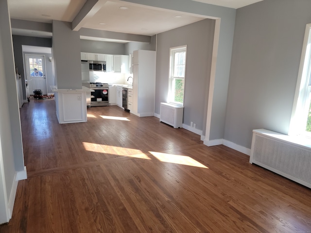 interior space featuring appliances with stainless steel finishes, white cabinetry, radiator, and hardwood / wood-style floors