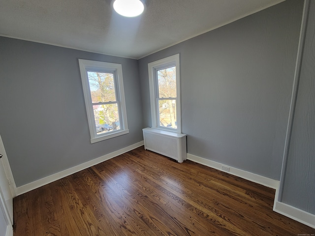 empty room featuring dark hardwood / wood-style flooring, radiator heating unit, and a textured ceiling