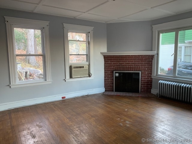 unfurnished living room featuring radiator, plenty of natural light, wood-type flooring, and a brick fireplace