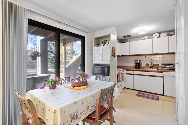 kitchen featuring backsplash, white appliances, sink, light tile patterned floors, and white cabinets