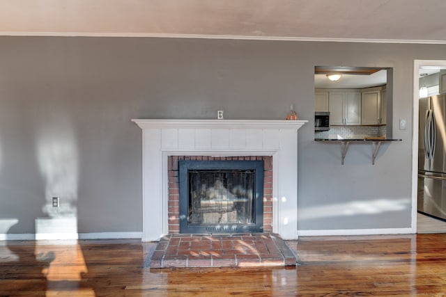 interior details featuring stainless steel appliances, a brick fireplace, tasteful backsplash, crown molding, and hardwood / wood-style floors