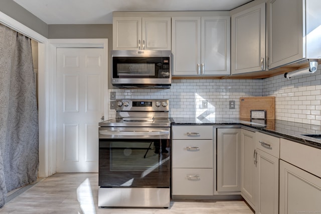 kitchen featuring appliances with stainless steel finishes, tasteful backsplash, light hardwood / wood-style flooring, and dark stone countertops