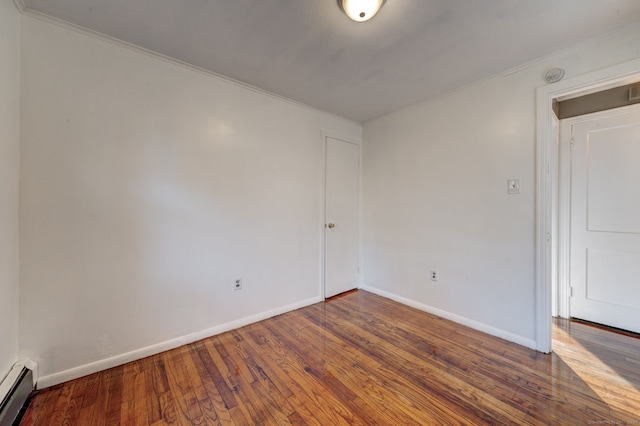 empty room with ornamental molding, dark wood-type flooring, and a baseboard heating unit