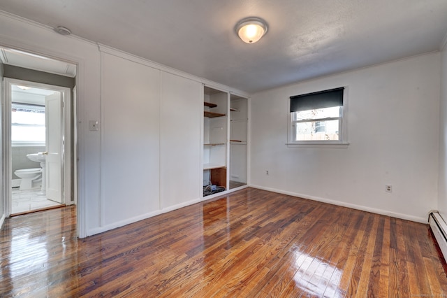 unfurnished bedroom with dark wood-type flooring, multiple windows, baseboard heating, and a closet