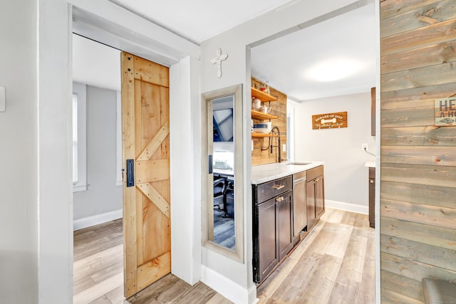 bar with dark brown cabinets, a barn door, light hardwood / wood-style flooring, and wooden walls