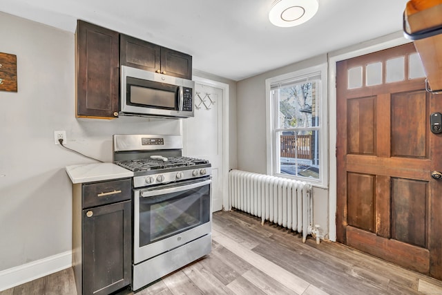 kitchen featuring radiator heating unit, light hardwood / wood-style flooring, light stone counters, dark brown cabinetry, and stainless steel appliances