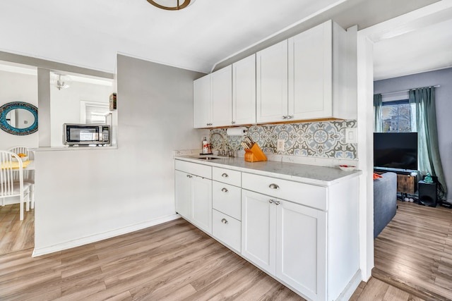 kitchen featuring white cabinetry, sink, light stone counters, backsplash, and light wood-type flooring