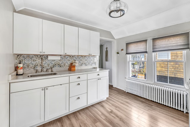 kitchen with backsplash, radiator, white cabinets, sink, and light hardwood / wood-style floors