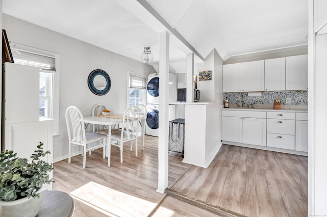 kitchen with backsplash, white cabinets, sink, stacked washer and dryer, and light hardwood / wood-style floors