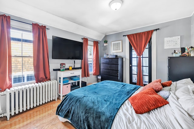 bedroom featuring light hardwood / wood-style floors, radiator heating unit, and multiple windows