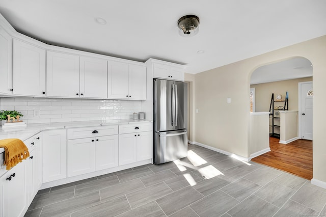 kitchen featuring light wood-type flooring, backsplash, light stone counters, white cabinetry, and stainless steel refrigerator