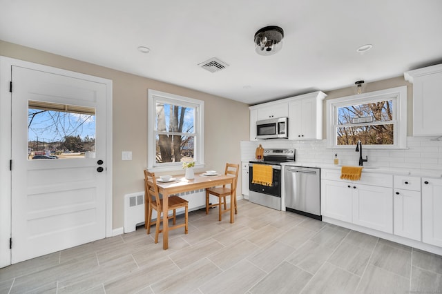 kitchen with white cabinets, plenty of natural light, radiator, and appliances with stainless steel finishes