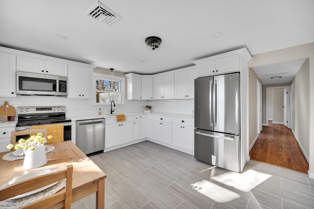 kitchen featuring backsplash, light hardwood / wood-style flooring, white cabinets, and stainless steel appliances