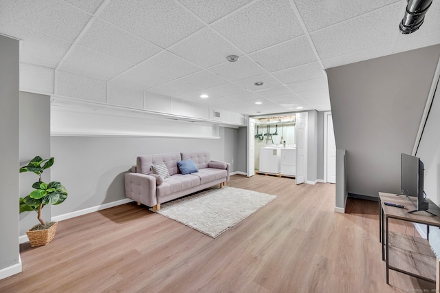 living room featuring a drop ceiling, light hardwood / wood-style flooring, and washing machine and clothes dryer