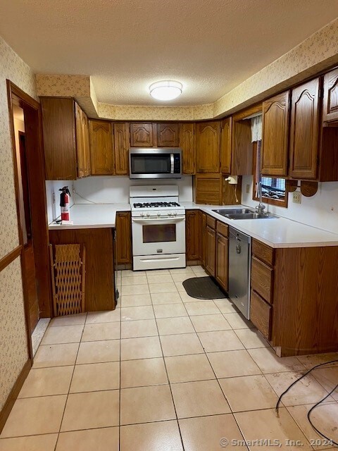 kitchen featuring a textured ceiling, light tile patterned flooring, sink, and appliances with stainless steel finishes