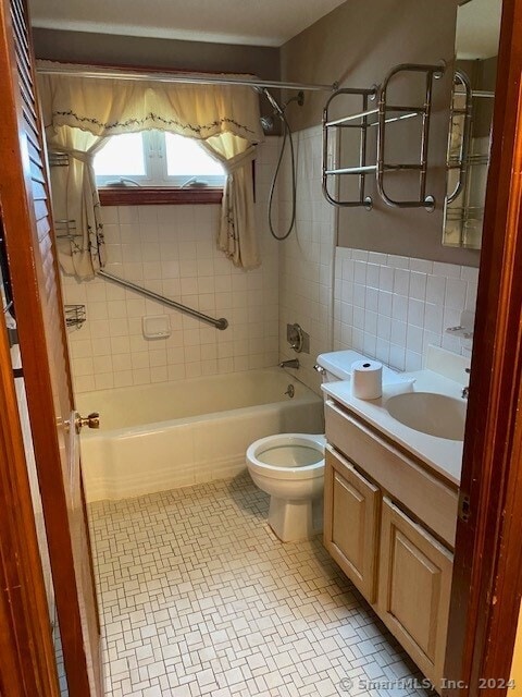 full bathroom featuring vanity, toilet, tiled shower / bath, and tile walls