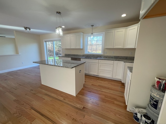 kitchen with decorative light fixtures, a kitchen island, white cabinetry, and light hardwood / wood-style flooring