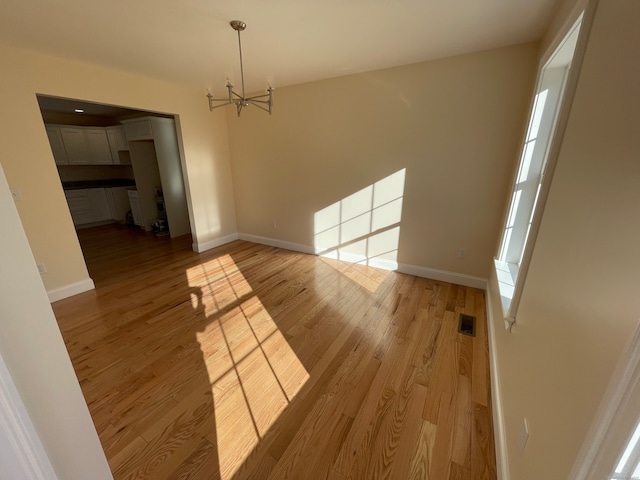 unfurnished dining area featuring light hardwood / wood-style floors and an inviting chandelier