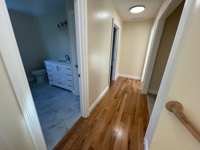 corridor with light wood-type flooring and sink