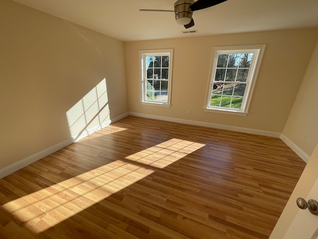 empty room featuring ceiling fan, a healthy amount of sunlight, and wood-type flooring