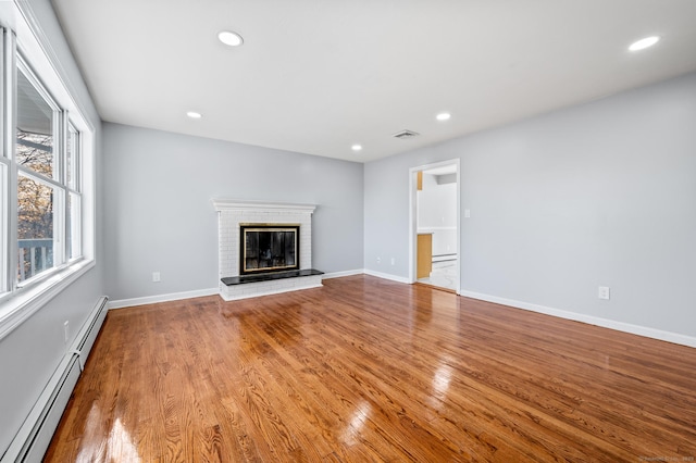 unfurnished living room with light hardwood / wood-style floors, a fireplace, and a baseboard heating unit