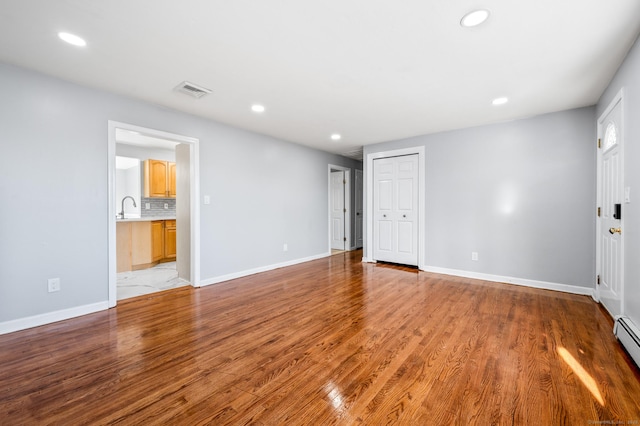 spare room featuring sink, a baseboard heating unit, and light wood-type flooring